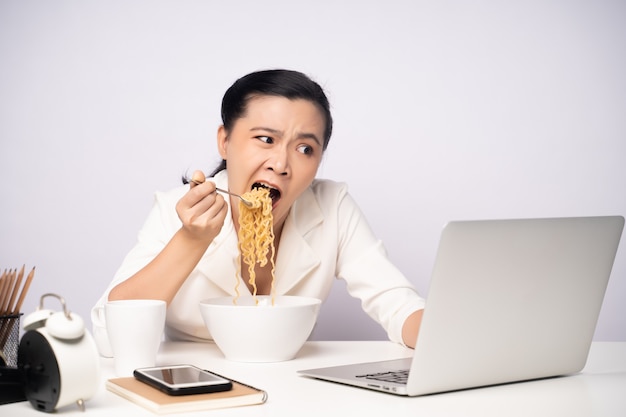 Donna asiatica che fa gli straordinari mangiando spaghetti istantanei in ufficio. Sconvolto imprenditrice occupato e affamato superlavoro.