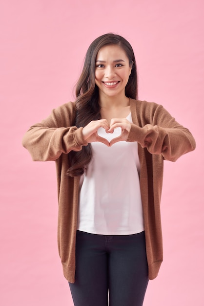 Donna asiatica che fa una forma di cuore con le mani, isolata su sfondo rosa