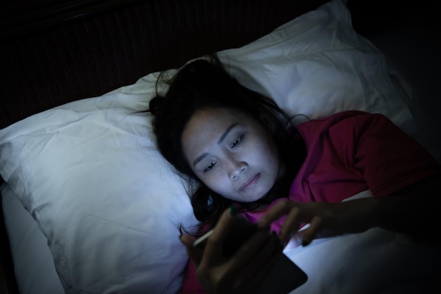 Donna asiatica che gioca sullo smartphone nel letto di notteThailand peopleAddict social media