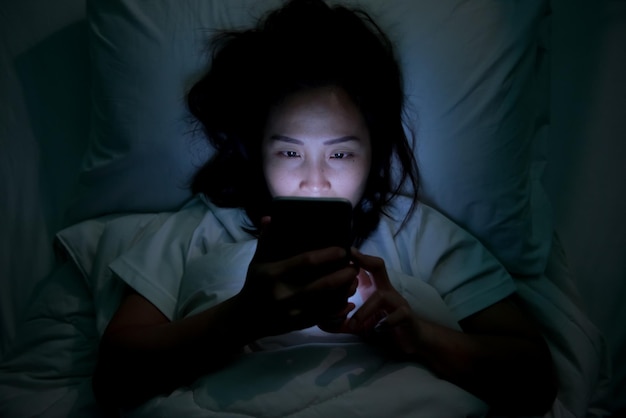 Donna asiatica che gioca sullo smartphone nel letto di notteThailand peopleAddict social media