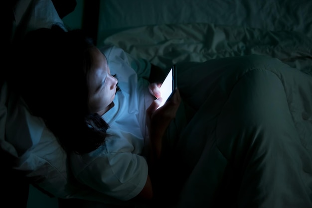 Donna asiatica che gioca sullo smartphone nel letto di notteThailand peopleAddict social media