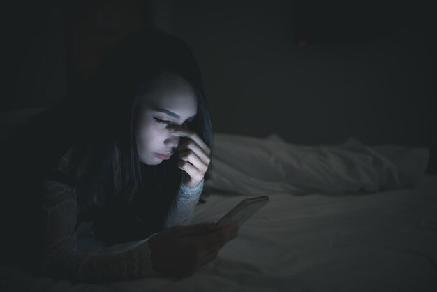 Donna asiatica che gioca sullo smartphone nel letto di notteThailand peopleAddict social media