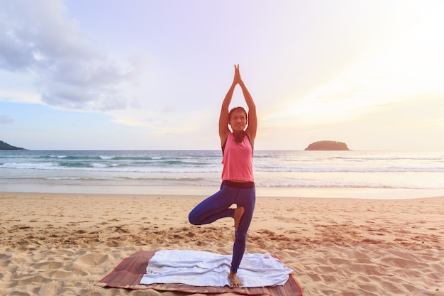 Donna asiatica che gioca yoga ed esercizio sulla spiaggia tropicale in Tailandia