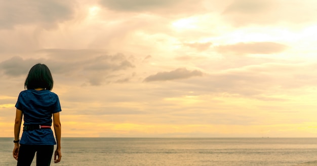 Donna asiatica che guarda il cielo di alba in spiaggia del mare. Il corridore si rilassa dopo aver corso sulla spiaggia tropicale. Uno stile di vita sano. La ragazza viaggia da sola in vacanza estiva. Vacanze sulla costa dell'oceano.