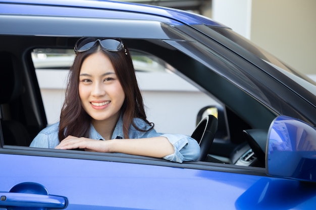 Donna asiatica che guida un'auto e sorride felicemente con felice espressione positiva durante il viaggio verso il viaggio, la gente gode ridendo di trasporto e guida attraverso il concetto