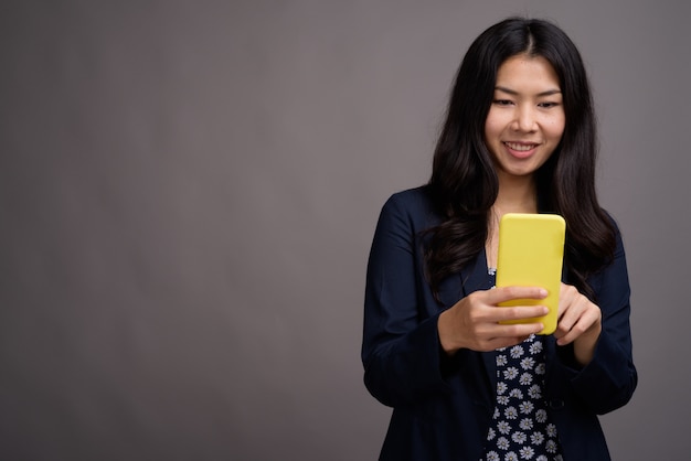 Donna asiatica che indossa abito blu e maglione cardigan mentre si utilizza il telefono cellulare contro lo spazio grigio