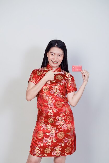 Donna asiatica che indossa il tradizionale abito cheongsam qipao che mostra la carta di credito per i concetti di acquisto del capodanno cinese.