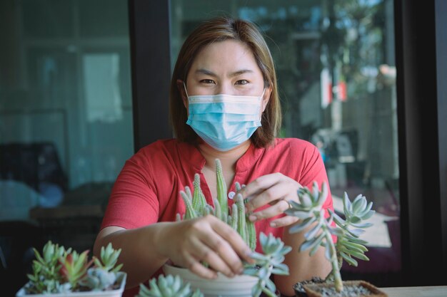 Donna asiatica che indossa la maschera di protezione che pianta cactus a casa