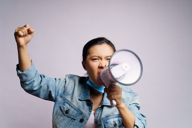 Donna asiatica che indossa la maschera protettiva che grida con il megafono isolato.