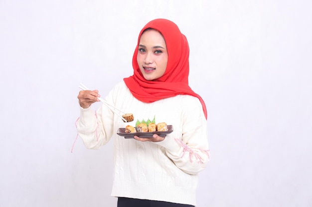 Donna asiatica che indossa un hijab sorride storto con la mano destra prende le bacchette e porta il piatto