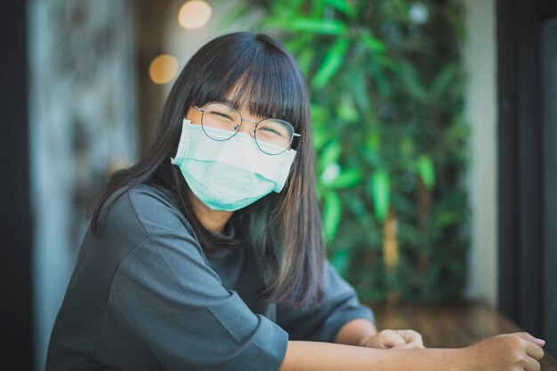 Donna asiatica che indossa una maschera di protezione seduta al tavolo del soggiorno