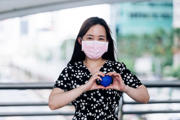 Donna asiatica che indossa una maschera e tiene in mano una palla blu Concetto di coronavirus