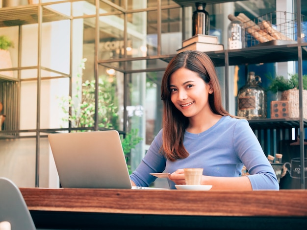 Donna asiatica che lavora con il computer portatile in caffetteria.