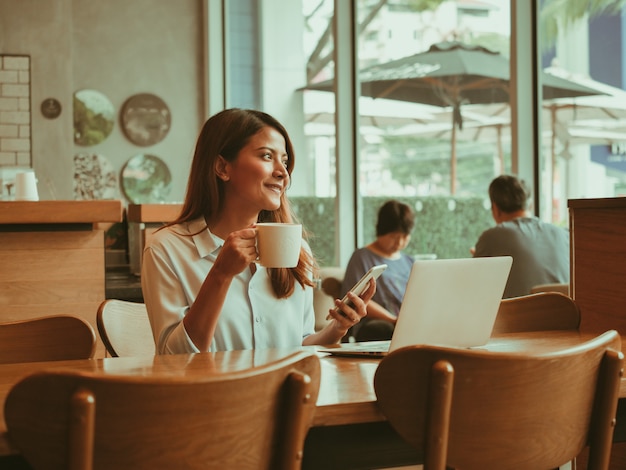 Donna asiatica che lavora con il computer portatile nel caffè della caffetteria