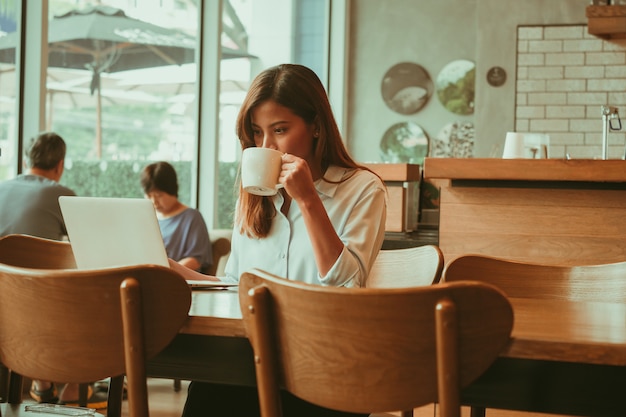 Donna asiatica che lavora con il computer portatile nel caffè della caffetteria