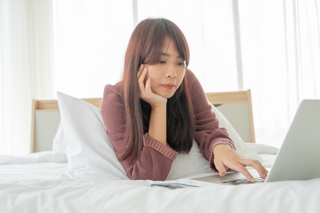 Donna asiatica che lavora con il computer portatile sul letto