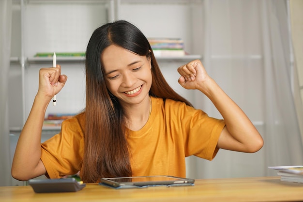 Donna asiatica che lavora da casa felice di guardare i profitti attraverso il computer