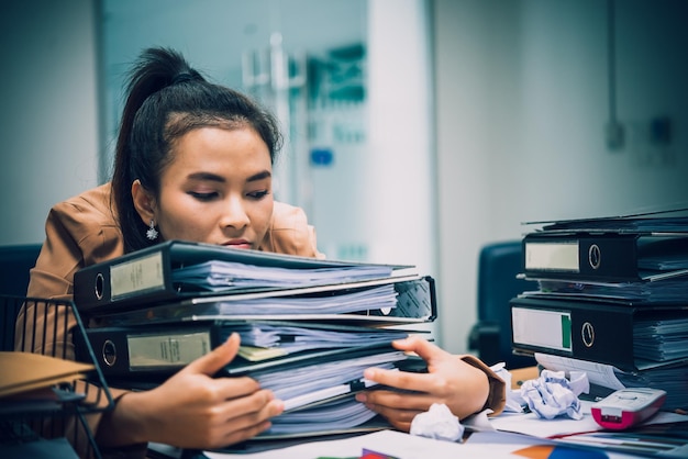 Donna asiatica che lavora in ufficio Giovane donna d'affari stressata dal sovraccarico di lavoro con un sacco di file sulla scrivania