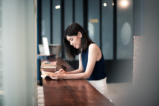 Donna asiatica che legge un libro al coffeeshop.