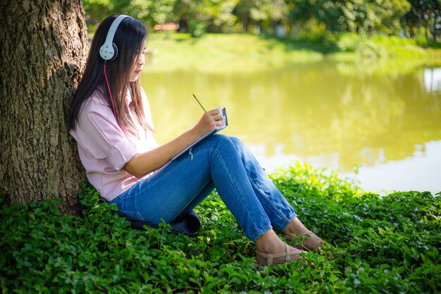 Donna asiatica che legge un libro e sorride nel parcoDonna asiatica soddisfatta che legge un libro in un parco