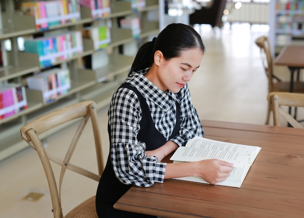 Donna asiatica che legge un libro nella libreria.