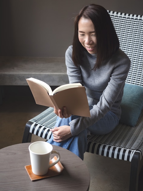 Donna asiatica che legge un libro sulla sedia