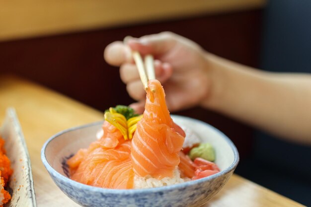 Donna asiatica che mangia il sashimi della fetta di salmone con riso nel ristorante giapponese