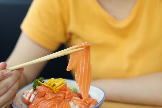 Donna asiatica che mangia il sashimi della fetta di salmone con riso nel ristorante giapponese