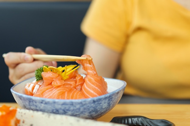 Donna asiatica che mangia il sashimi della fetta di salmone con riso nel ristorante giapponese