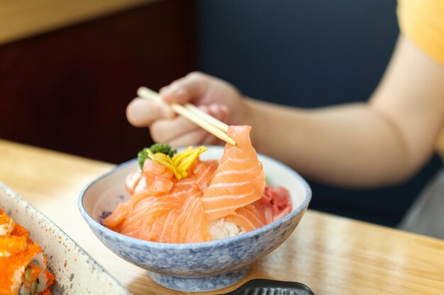 Donna asiatica che mangia il sashimi della fetta di salmone con riso nel ristorante giapponese