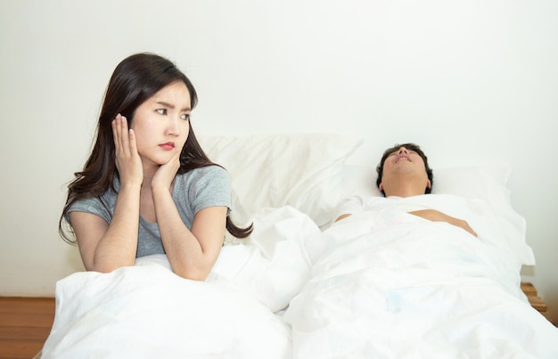 Donna asiatica che ottiene disturbata e infastidita dal sonno dell'uomo e russare sul letto