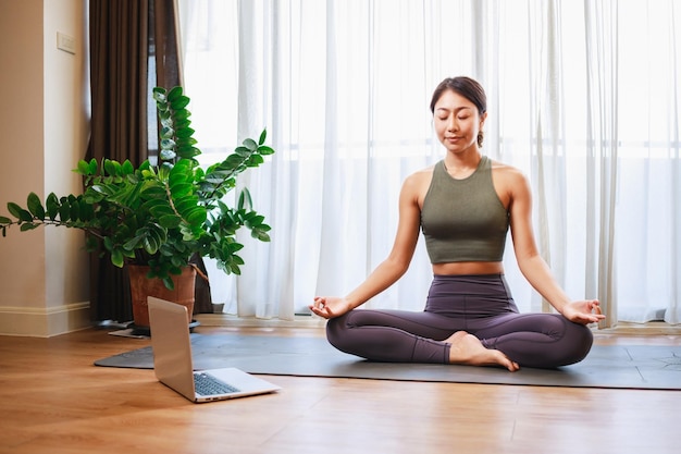 Donna asiatica che pratica yoga dal corso online di yoga in una videoconferenza su un laptop a casa