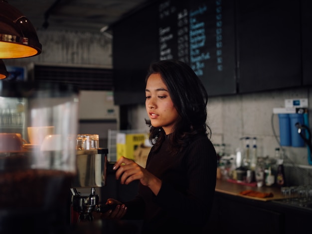 Donna asiatica che produce caffè con la macchina del caffè in caffè