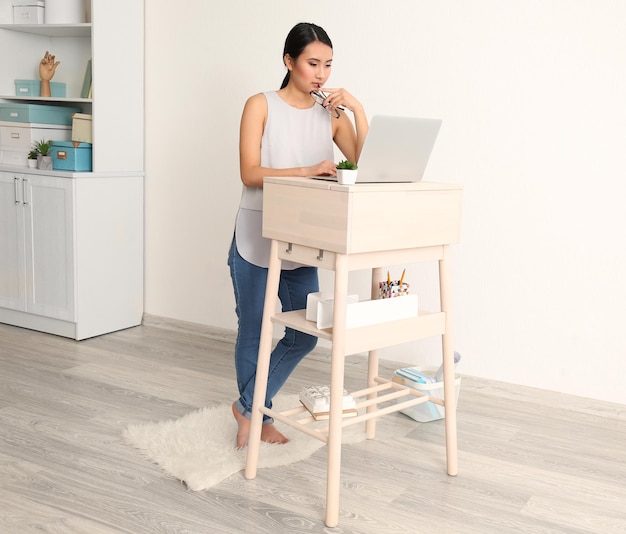 Donna asiatica che scrive sul computer portatile sul posto di lavoro in piedi