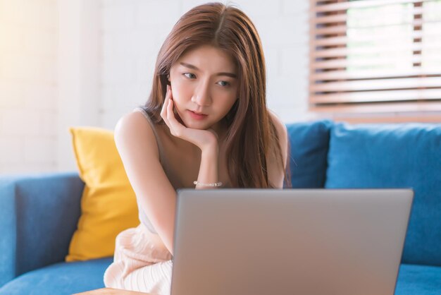 Donna asiatica che si rilassa seduta sul divano usando il computer, non nel soggiorno.