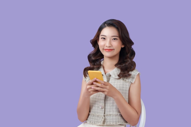 Donna asiatica che si siede sul divano usando il suo telefono con una felice espressione