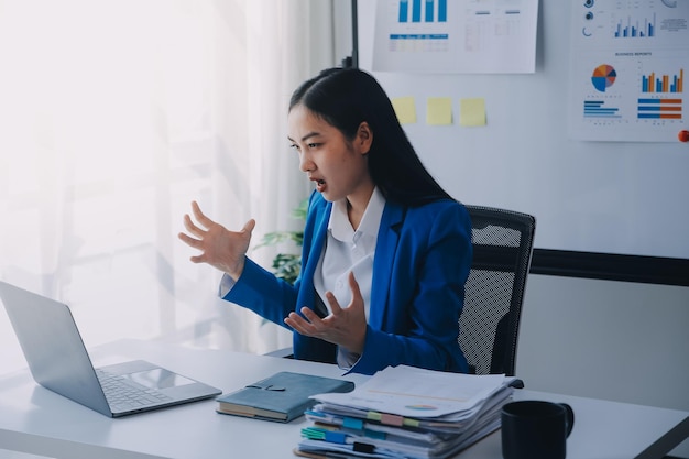 Donna asiatica che soffre di emicrania, sovraccarica di lavoro, donna d'affari, finanziera, mentre lavora con il portatile e il tablet in un ufficio moderno.