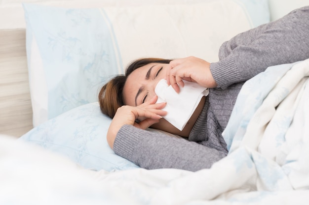 Donna asiatica che soffre di influenza e sdraiata sul letto con il tessuto