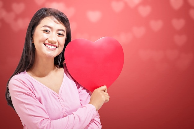 Donna asiatica che tiene il cuore rosso con una parete colorata. San Valentino