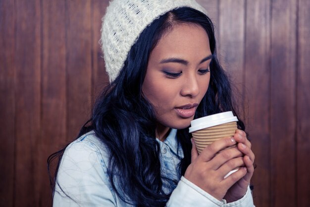 Donna asiatica che tiene tazza eliminabile contro la parete di legno