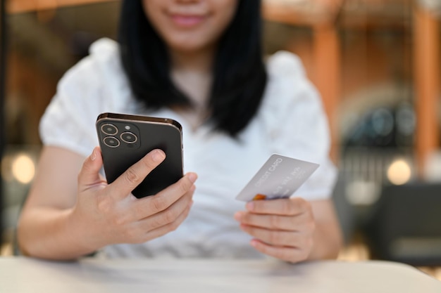 Donna asiatica che usa il suo smartphone per pagare le bollette online che tengono smartphone e carta di credito