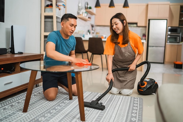 Donna asiatica che usa l'aspirapolvere per pulire la casa con il suo partner