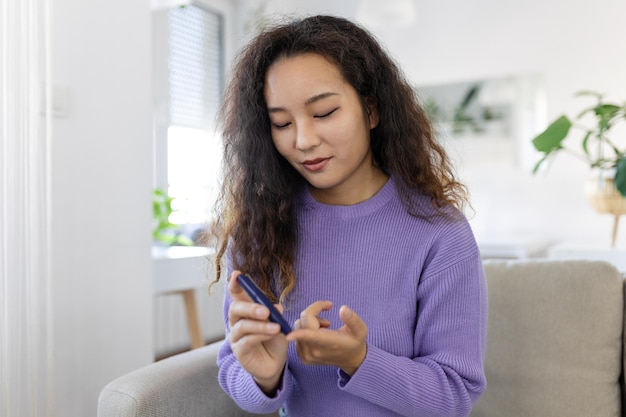 Donna asiatica che usa la lancetta sul dito Donna che esegue il test della glicemia a casa in un soggiorno