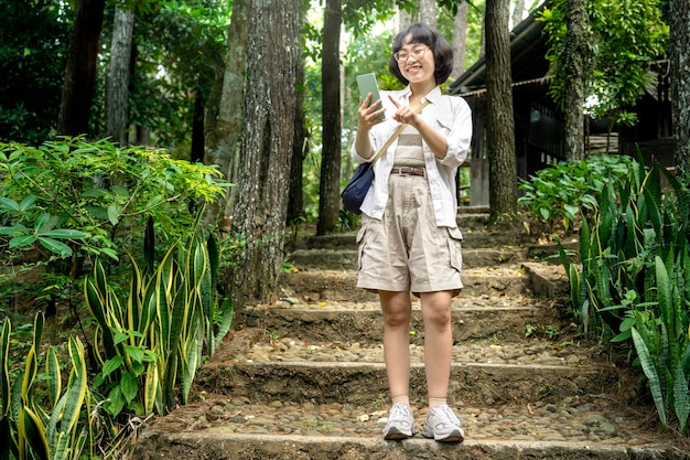 Donna asiatica che usa un cellulare mentre cammina nella foresta