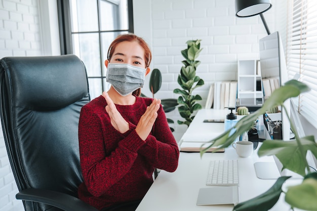 Donna asiatica che usando maschera che si siede sulla scrivania