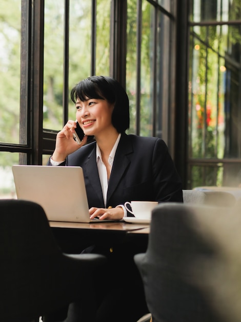 Donna asiatica che utilizza computer portatile e che beve caffè nel caffè della caffetteria