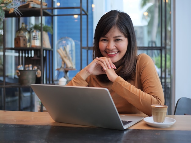 Donna asiatica che utilizza computer portatile nel caffè della caffetteria