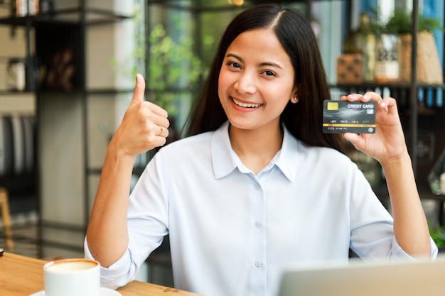 Donna asiatica che utilizza la carta di credito che compera online nel caffè della caffetteria