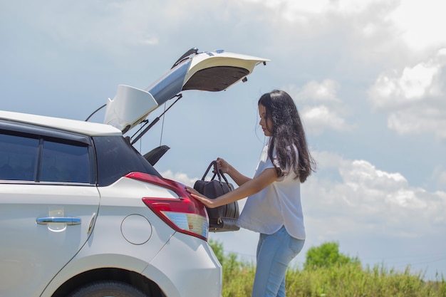 Donna asiatica che va in vacanza caricando il bagagliaio della macchina con valigie da viaggio