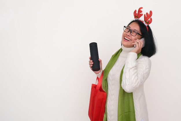 Donna asiatica con abiti bianchi caldi e fascia per i capelli di Natale che fa una telefonata